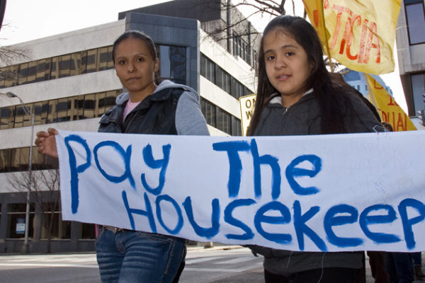 Woman and child holding up "Pay the Housekeepers" protest sign